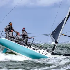 Equipaggio su barca a vela con spinnaker in azione, solcando onde agitate.