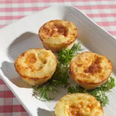 Små, gyllene potatis i muffinsform, serverade med färska örter på en vit bricka. Perfekt som tillbehör eller plockmat.