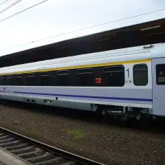 Biało-niebieski wagon PKP Intercity z żółtym pasem, numerem "1" i oknami. To wagon bez przedziałów, idealny na podróż.