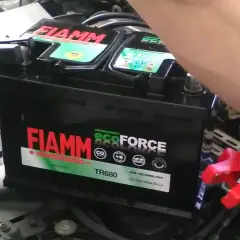 Ręce podłączają kable do akumulatora FIAMM ecoFORCE. Widoczne oznaczenia na akumulatorze, w tym model TR680 i technologia AFB.