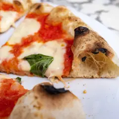 Kawałki pysznej pizzy neapolitańskiej z ciągnącym się serem i świeżą bazylią.