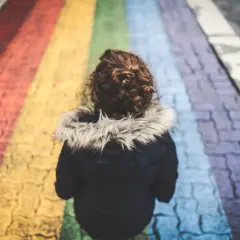 Dziecko z kręconymi włosami idzie po tęczowym przejściu dla pieszych.