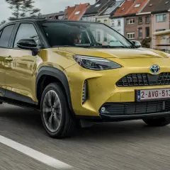 Żółty Toyota Yaris Cross używane na drodze, z czarnym dachem i felgami. W tle widać zabudowania miejskie.
