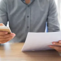 Mężczyzna trzyma telefon i dokument, sprawdzając potwierdzenie przelewu.