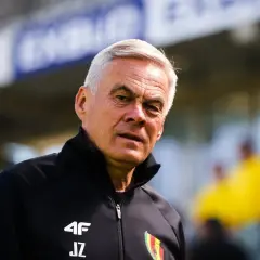 Jacek Zieliński, doświadczony trener, w czarnej kurtce z logo 4F i inicjałami JZ, na tle stadionu.