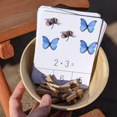 Karty pracy z owadami i zadaniami matematycznymi, np. 2+3=, w miseczce z klamerkami.