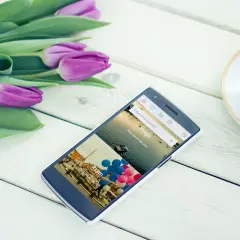Telefon z aplikacjami przydatnymi w podróży, pokazujący Praga i Rzym. Obok bukiet tulipanów i filiżanka kawy.