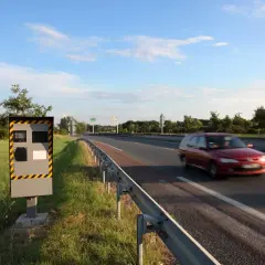 Un radar de chantier surveille la route. Une voiture rouge passe vite.