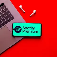 Laptop, telefon z logo Spotify Premium i słuchawki na czerwonym tle.