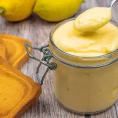Vaso di vetro pieno di cremoso lemon curd, pronto per essere gustato con biscotti e limoni freschi.