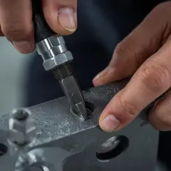 Precyzyjne dokręcanie śruby w metalowym elemencie. Dłoń trzyma narzędzie, a palce stabilizują element, by nok bomu zapewnił idealne dopasowanie.