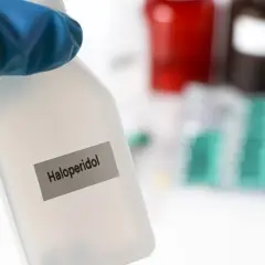Blauer Handschuh hält Flasche mit der Aufschrift "Haloperidol". Im Hintergrund sind Medikamentenpackungen zu sehen.