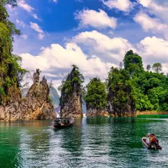Khao Sok nationalpark med sina dramatiska kalkstensklippor och smaragdgröna vatten. Två små båtar glider fram på sjön.