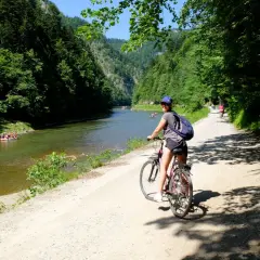 Dziewczyna na rowerze na malowniczej trasie rowerowej w Szczawnicy. W tle Dunajec z tratwami.