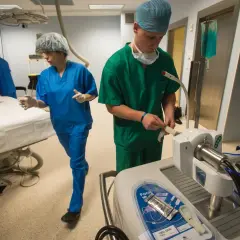 Chirurdzy w zielonych i niebieskich fartuchach w sali operacyjnej, przygotowujący pacjenta.