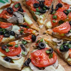 Kawałki pysznej, **zdrowej pizzy** z pomidorami, oliwkami i pieczarkami na drewnianej desce.