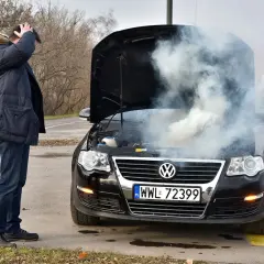 Mężczyzna zrezygnowany patrzy na dym spod maski i czuje zapach spalenizny. Awaria Volkswagena na poboczu.