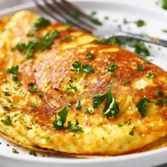 En gyllene omelett, perfekt för ett snabbt omelett recept, toppad med färsk persilja och serverad på en vit tallrik med en gaffel.