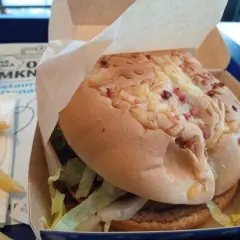 Pyszny lumberjack burger z McDonald's w papierowym opakowaniu, obok złociste frytki.
