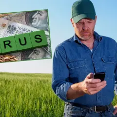 Rolnik w polu sprawdza telefon. Obok zboże, banknot 100 zł i kostki z napisem "KRUS". Ubezpieczony rolnik dba o swoje interesy.