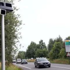Un radar leurre sur un poteau, avec des voitures sur la route et un panneau de signalisation.
