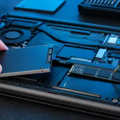 Wymiana dysku w laptopie: ręka trzyma nowy dysk SSD, druga dokręca śrubkę precyzyjnym śrubokrętem.
