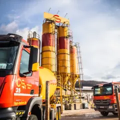 Zwei Betonmischer stehen vor hohen Silos einer Betonmischanlage. Die hgt tragschicht ist bereit für den Transport.