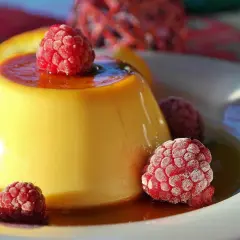 Crème aux œufs onctueuse, nappée de caramel et garnie de framboises givrées. Un délice visuel et gustatif.