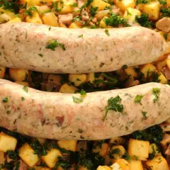 Deux andouillettes au four, dorées et savoureuses, reposent sur un lit de pommes de terre sautées et de persil frais. Un plat réconfortant prêt à être dégusté.