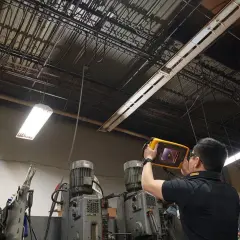 Técnico revisa el techo de una fábrica con un dispositivo para detectar una fuga de aire.