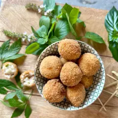 Goldbraune Arancini in einer Schale, umgeben von frischem Basilikum. Was isst man zu Arancini? Oft mit einer leichten Sauce oder einfach so!
