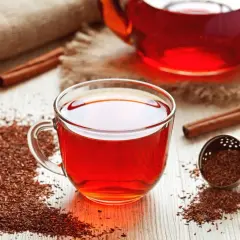 Aromatic rooibos właściwości: napar w szklance, susz, laska cynamonu i zaparzacz na drewnianym blacie.