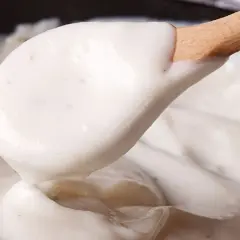 Cremosa bechamel vegana servida en una cuchara de madera, lista para dar un toque delicioso a tus platos.