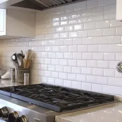 A clean kitchen backsplash installation with white subway tiles, a red stand mixer, and cooking utensils.