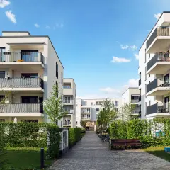 Immeubles modernes avec balcons, chemin pavé, verdure. Une location avec promesse de vente, un lieu de vie prometteur.