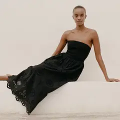 Mujer con vestido negro sin tirantes y falda larga con bordados florales, un ejemplo de moda ecológica.