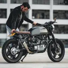 Uomo con moto custom grigia. La sella in pelle marrone ha una **godronatura** a rombi.