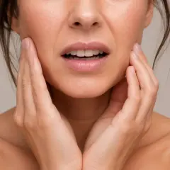 Mujer con expresión de dolor, tocándose la mejilla. Podría ser dolor después de empaste.