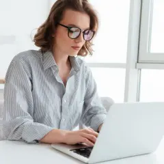 Kobieta w okularach pracuje na laptopie, szukając informacji o **santander zamknięcie konta**.