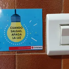 Un cartel azul con una bombilla amarilla y el texto "CUANDO SALGAS, APAGA LA LUZ" junto a un interruptor blanco.
