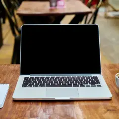 Laptop z pustym ekranem, notatnik z długopisem i filiżanka kawy na drewnianym stole. Idealne miejsce do pracy nad projektem z wykorzystaniem dysku hybrydowego.