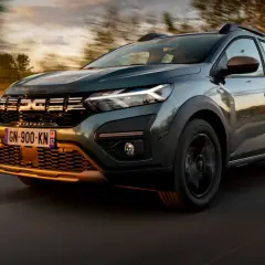 Zielony Dacia Sandero Stepway pędzi po drodze o zachodzie słońca, otoczony rozmazanymi drzewami i mglistym krajobrazem.