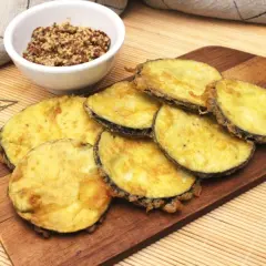 Berenjenas rebozadas doradas y crujientes, servidas en tabla de madera con un cuenco de mostaza.