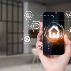 Dłoń trzyma smartfon z ikoną domu i otaczającymi go symbolami. To interfejs aplikacji spectrum smart, zarządzającej inteligentnym domem.