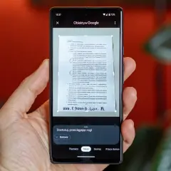 Ręka trzyma smartfon, na ekranie którego działa skaner dokumentów. Aplikacja Obiektyw Google skanuje tekst z papierowego dokumentu.