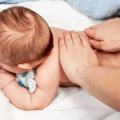 Delikatne oklepywanie pleców niemowlaka, by pomóc mu przy kaszlu. Ręce rodzica wykonują łagodne ruchy na malutkich pleckach.