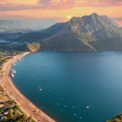 Widok z lotu ptaka na wybrzeże Turcji. Piękne turkusowe morze, piaszczysta plaża z leżakami i góry w tle o zachodzie słońca.