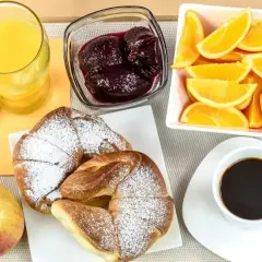 Pyszne śniadanie kontynentalne: rogaliki z cukrem pudrem, sok pomarańczowy, kawa, dżem, pomarańcze i jabłko.