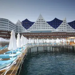 Widok na Orange County Resort Alanya z pomostem pełnym leżaków i parasoli, z błękitnym morzem w tle.