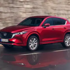 Czerwony suv Mazda CX-5 jedzie po mokrej drodze, odbijając się w kałuży.